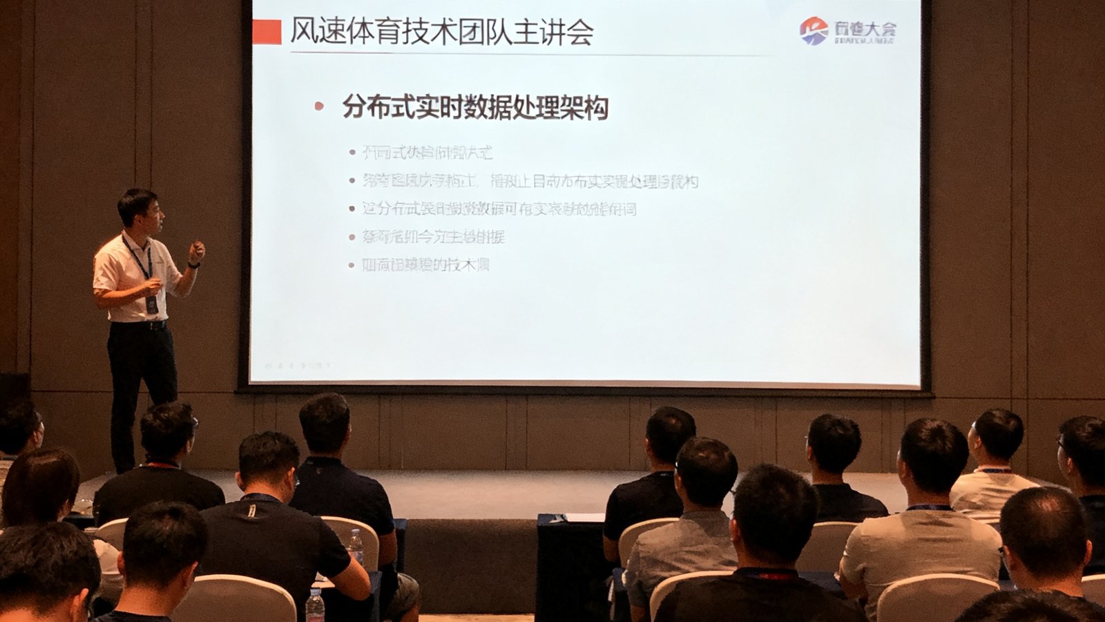 风速体育技术团队在行业大会上演讲的照片：主讲人在台上讲解分布式实时数据处理架构的PPT，台下坐满了参会者